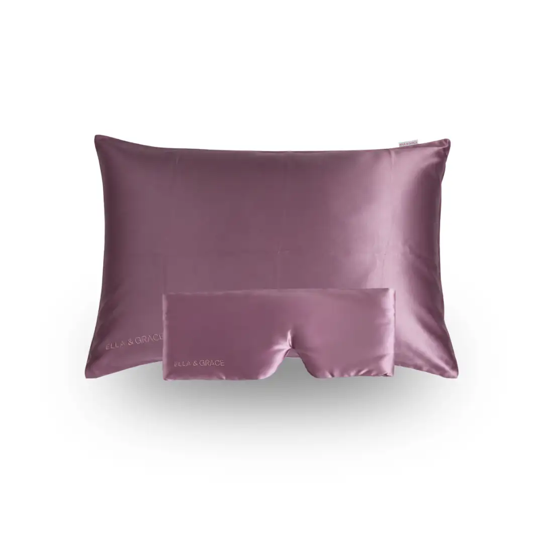 A soft blush pink silk pillowcase with a matching silk sleep eye mask from ELLA & GRACE displayed on a clean white background.